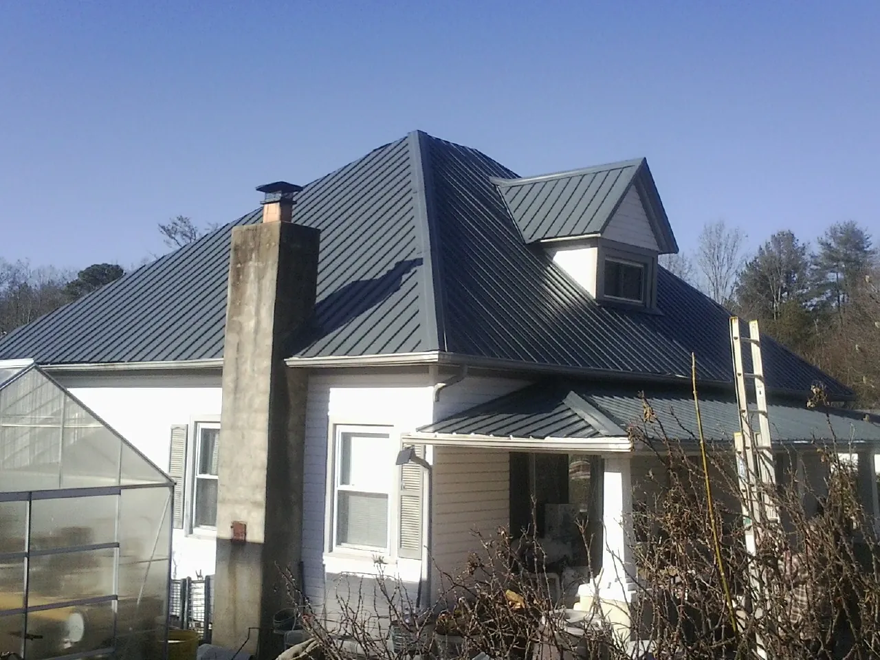 Dark blue standing seam metal roof on a white farmhouse with dormer — Slate & Tile Roof Repair by Roofing Brothers in Calvin