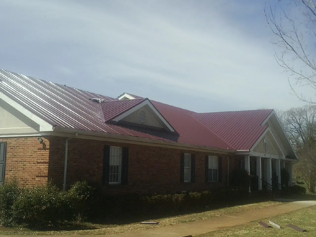 Red metal roof with gabled entries on a long brick building, from a Hail Damage Roof Repair job in Calvin