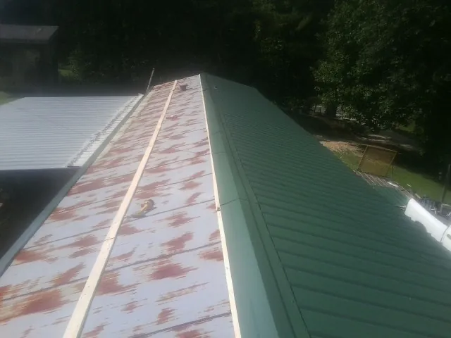 Old rusted panels beside newly installed green metal roofing — Wind Damage Roof Repair by Roofing Brothers in Calvin