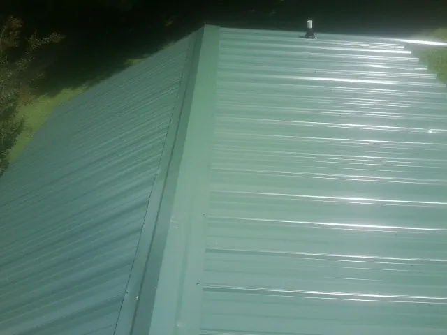 New green metal panels meeting at the ridge of a roof — Flat Roof Repair work by our crew in Calvin