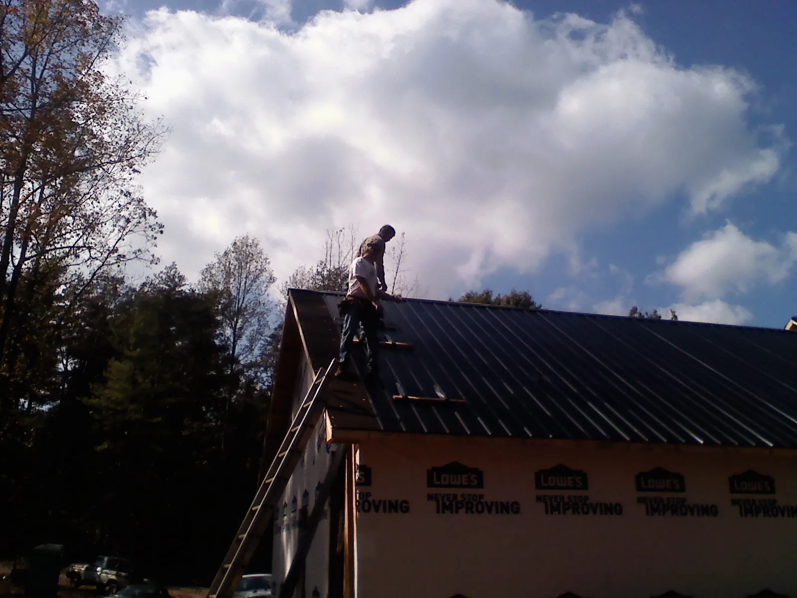 Roofer fastening dark metal panels high against a cloudy sky, from a Roof Inspection job in Calvin