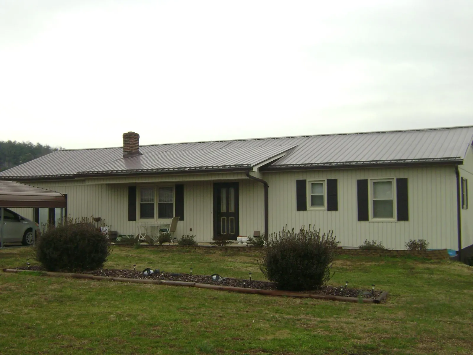 Brown metal roof on a cream sided ranch home with a brick chimney in Calvin