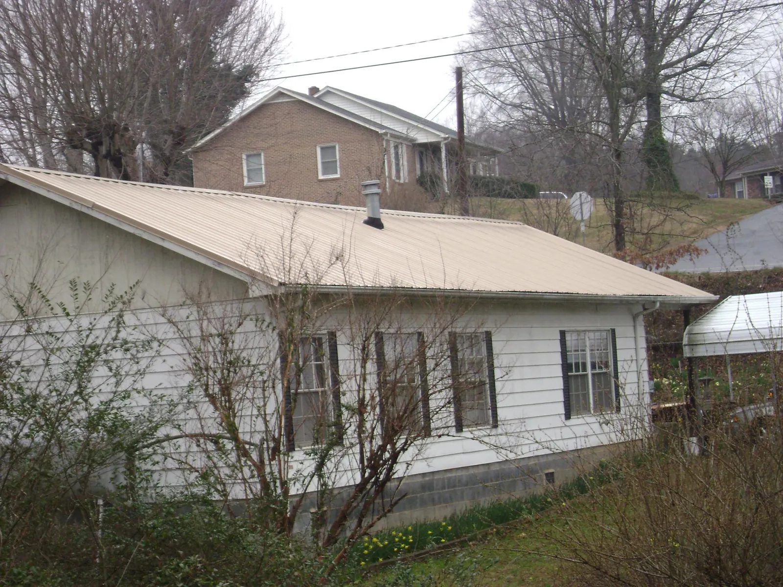 Tan metal roof on a white sided house set into a hillside — Commercial Roofing by Roofing Brothers in Calvin