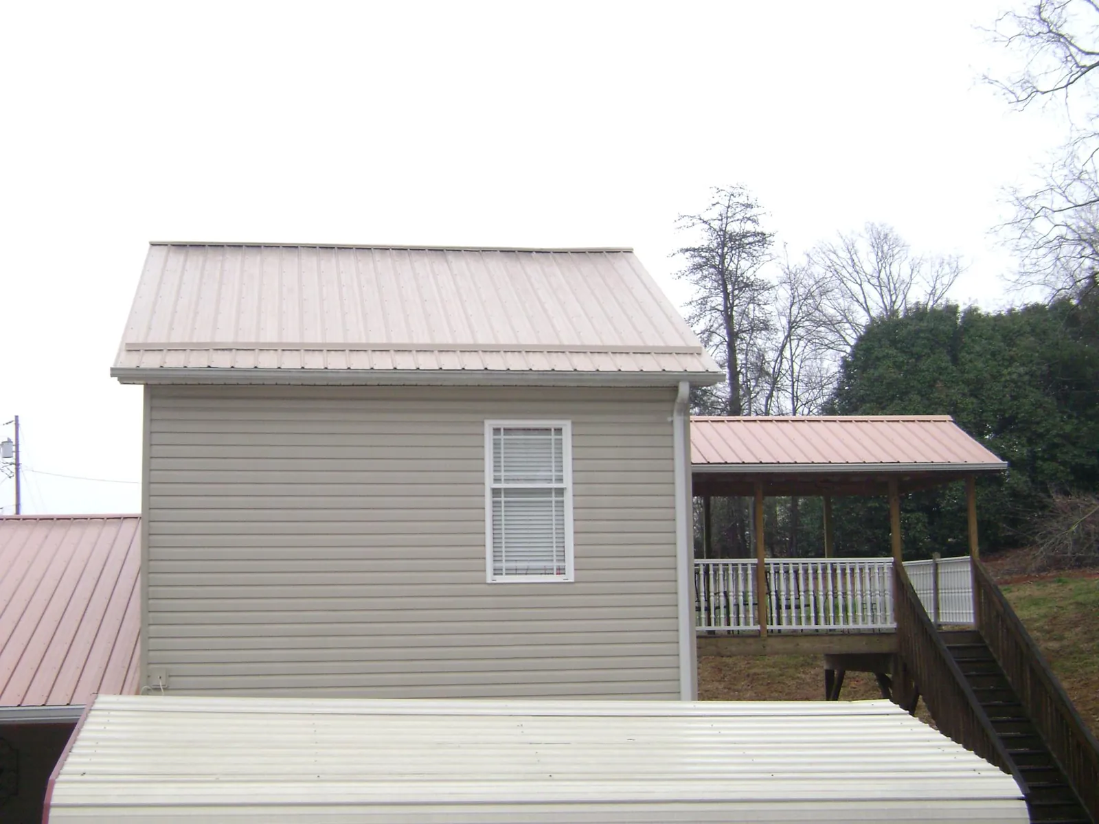 Tan metal roofs on a two story addition and attached porch, from a Roof Replacement job in Calvin